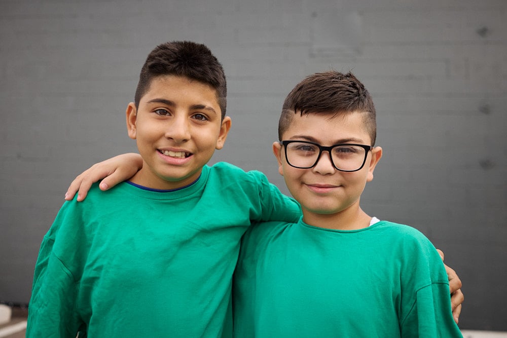 Two kids in green t-shirts smile at the camera